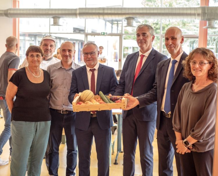 Lors de la présentation de l'expérimentation de centralisation des achats de denrées alimentaires, Philippe Dupouy tient une cagette de légumes, aux côtés du préfet du Gers et du  Directeur Académique des Services de l'Éducation Nationale